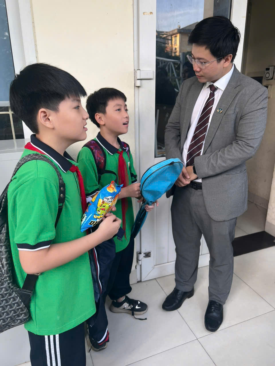 A person in a suit standing next to a group of boysDescription automatically generated