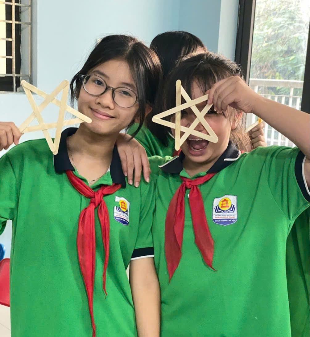 Two girls in green uniforms holding sticks over their eyesDescription automatically generated