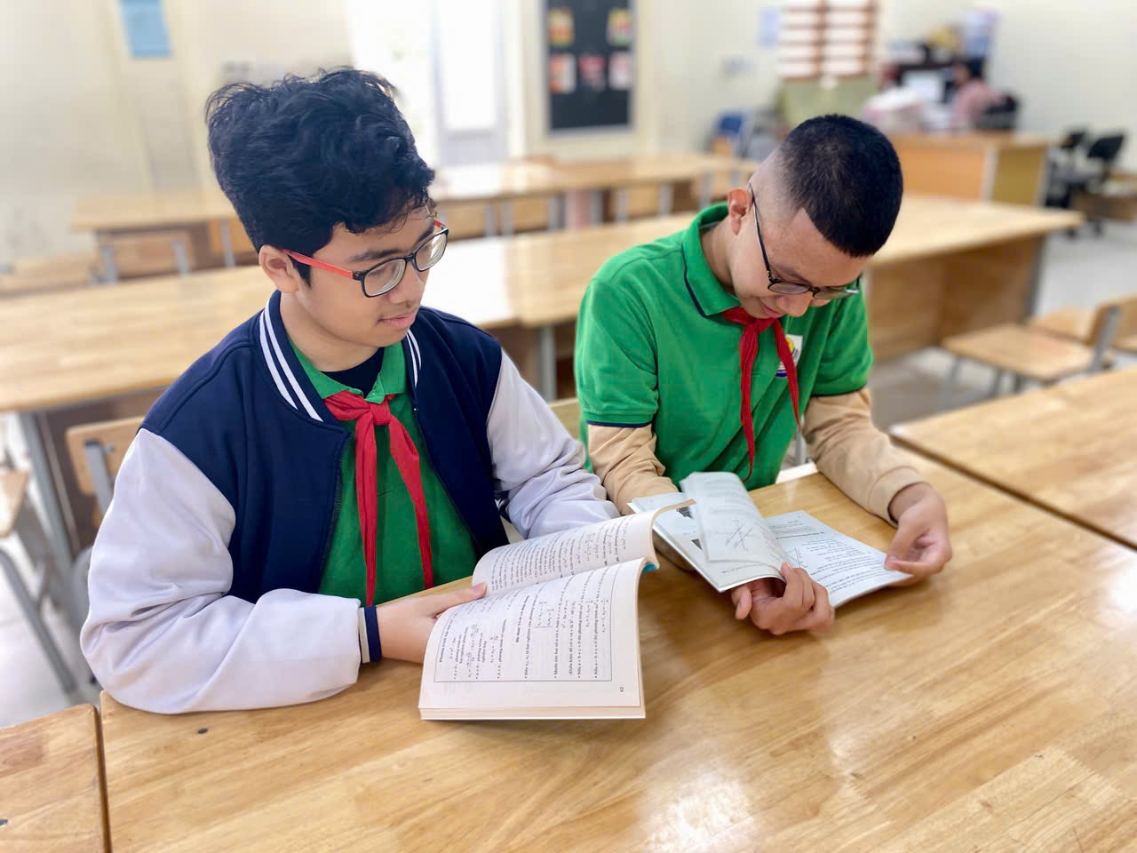 Two boys sitting at a table reading books

Description automatically generated