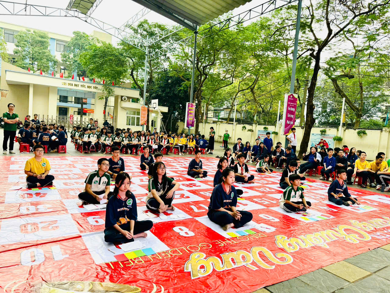A group of people sitting on a red and white mat

Description automatically generated
