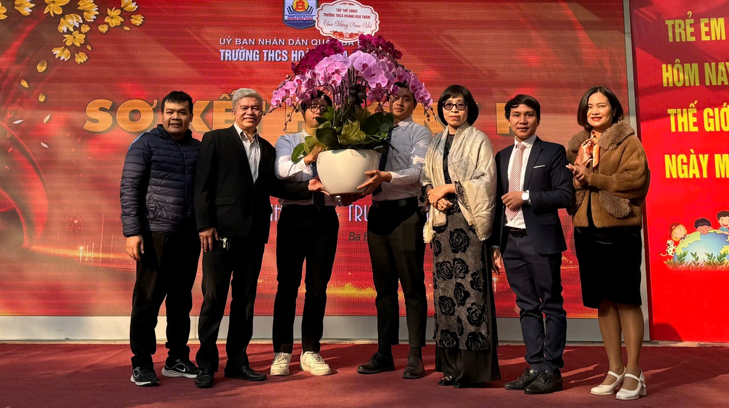 A group of people standing together holding a pot of flowersDescription automatically generated