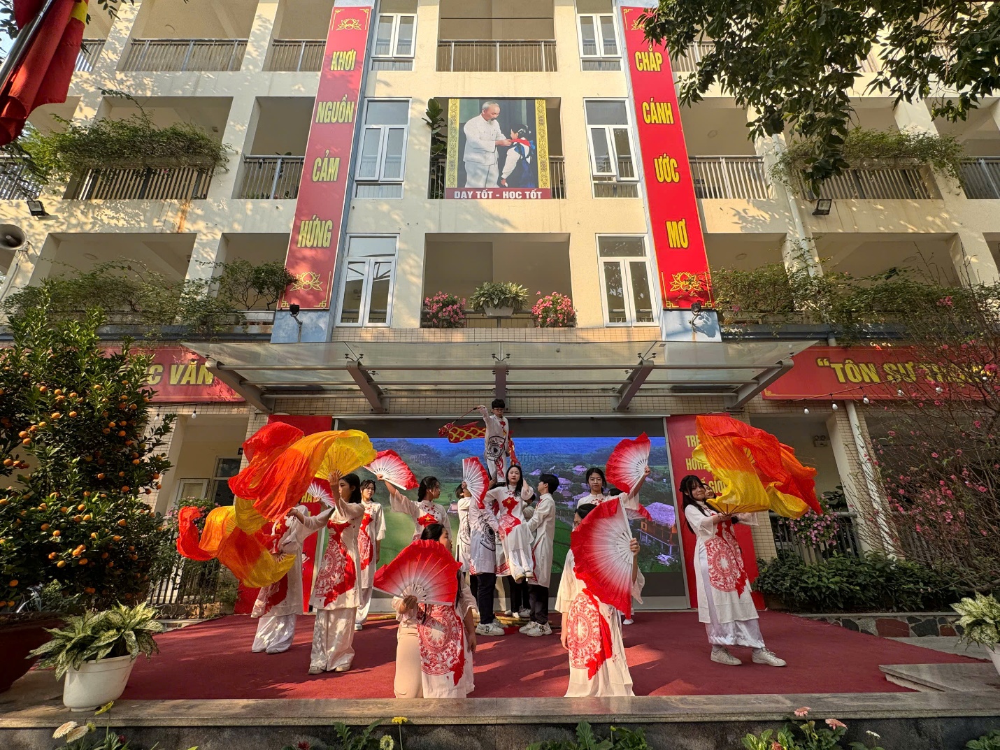 A group of people in white dresses with red and yellow fansDescription automatically generated