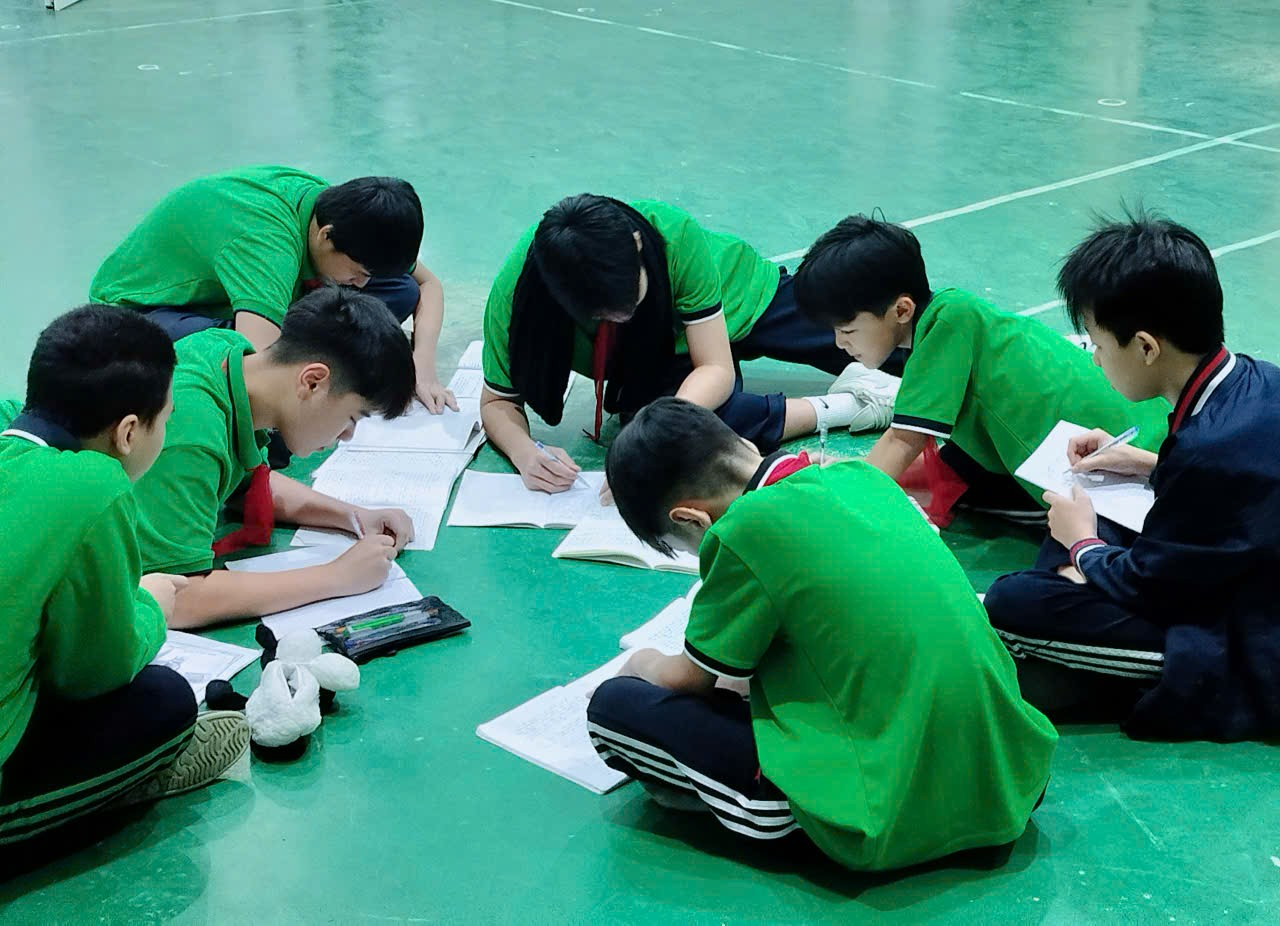 A group of boys in green shirts studying on the floor

Description automatically generated