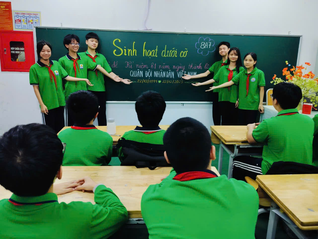 A group of people in green shirts in front of a chalkboard

Description automatically generated