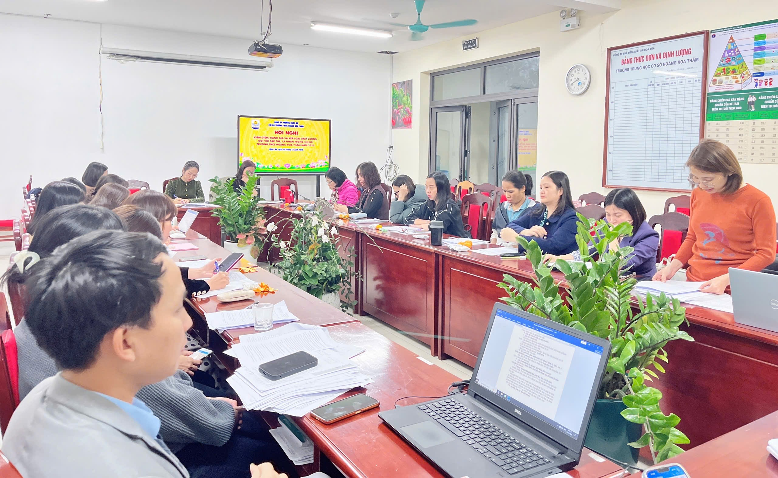A group of people sitting at long tables in a room with computers
Description automatically generated