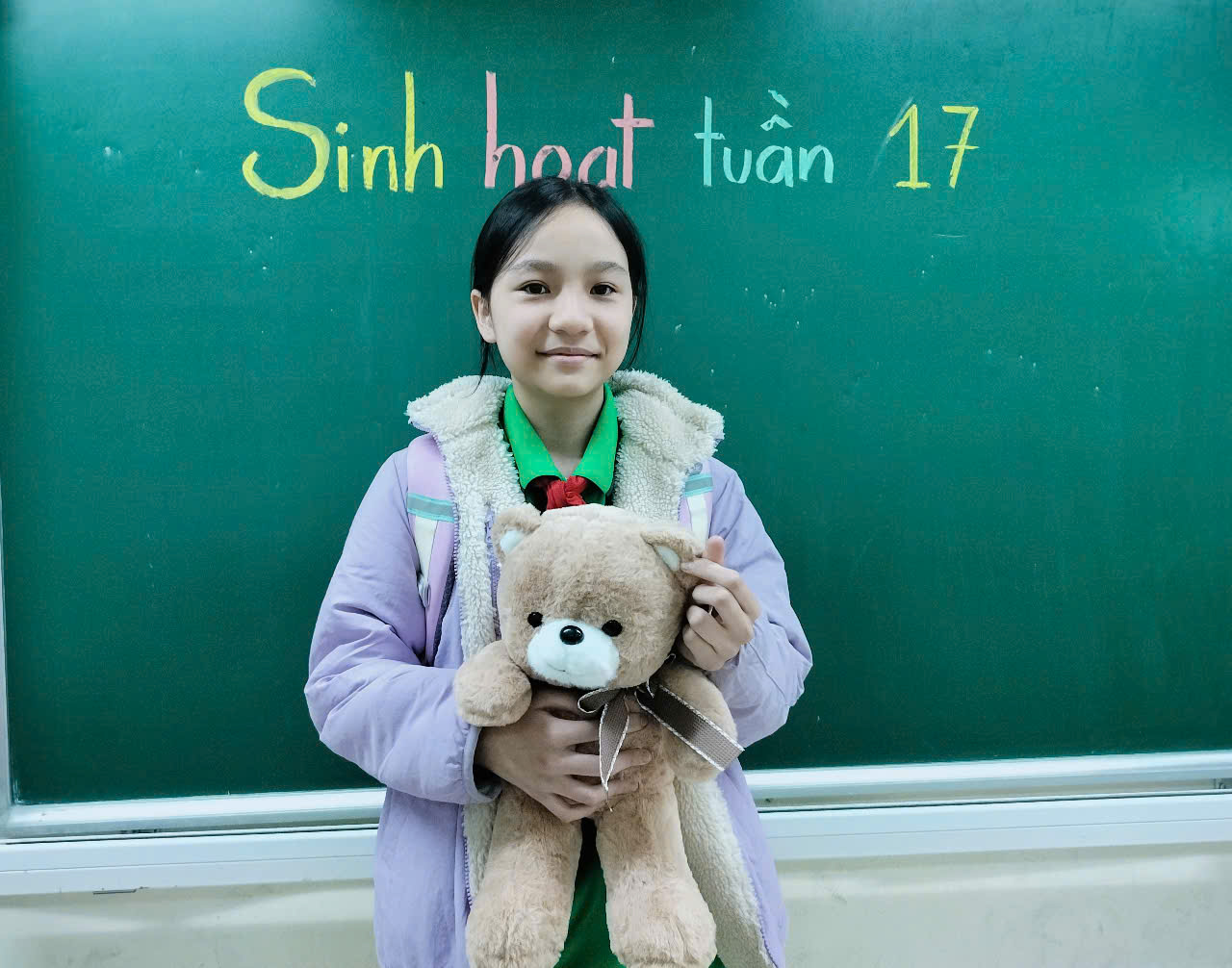 A child holding a teddy bear in front of a chalkboard

Description automatically generated