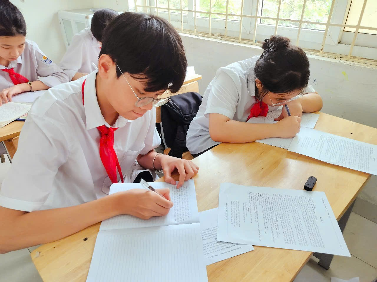A group of students sitting at a table writing on paper

Description automatically generated