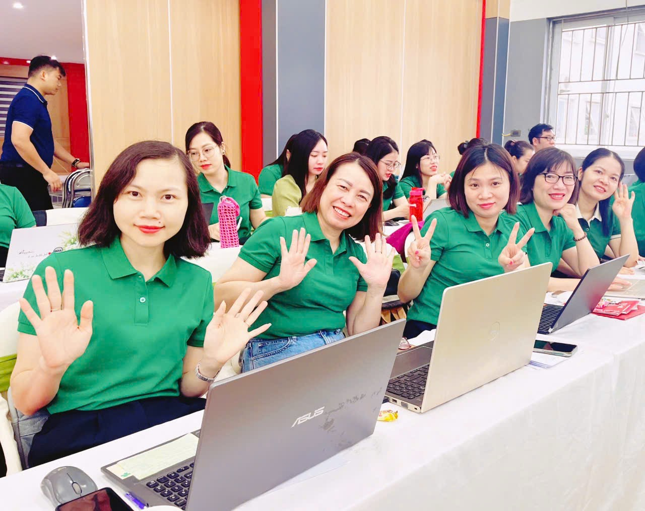 A group of women in green shirts sitting at a table with laptops

Description automatically generated