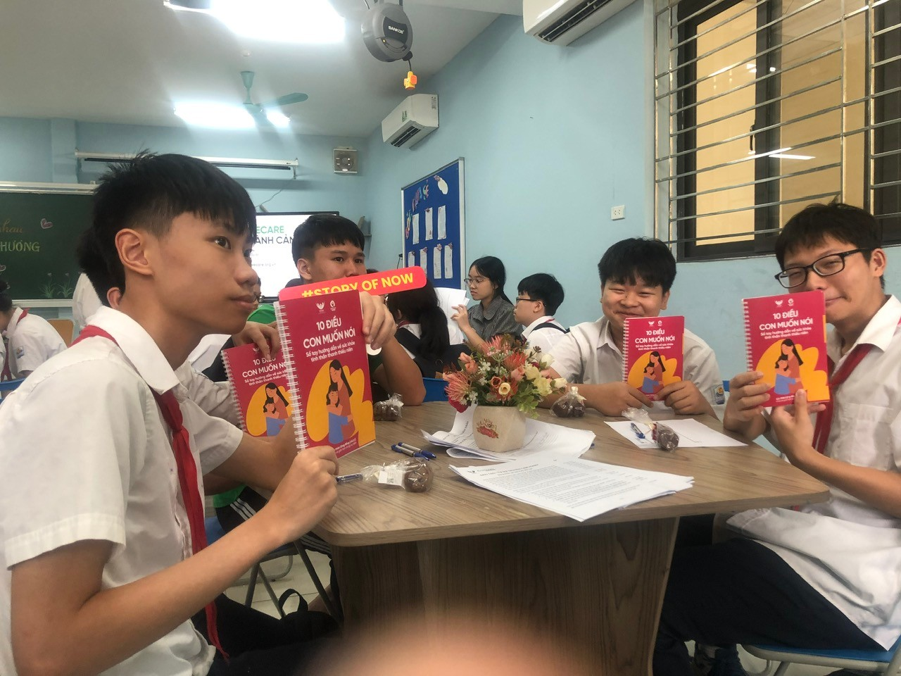 A group of people sitting at a table holding up books
Description automatically generated
