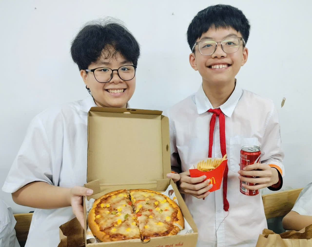Two people holding a pizza and a soda

Description automatically generated