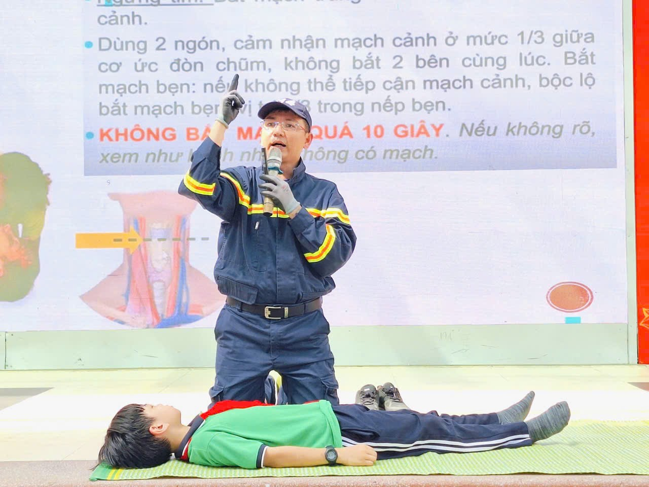 A person in uniform holding a microphone and pointing at a child lying on his backDescription automatically generated