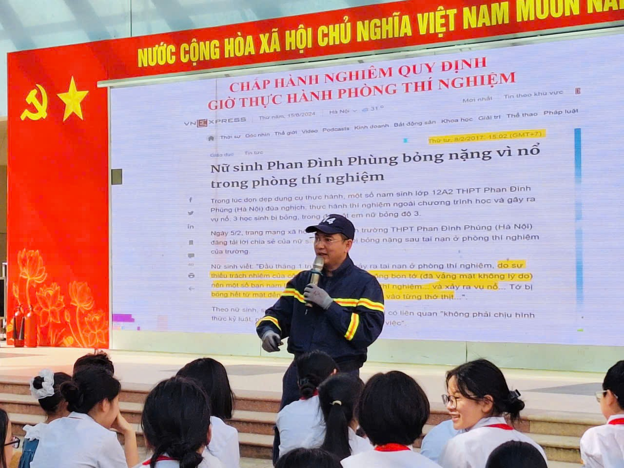A person speaking into a microphone in front of a large signDescription automatically generated