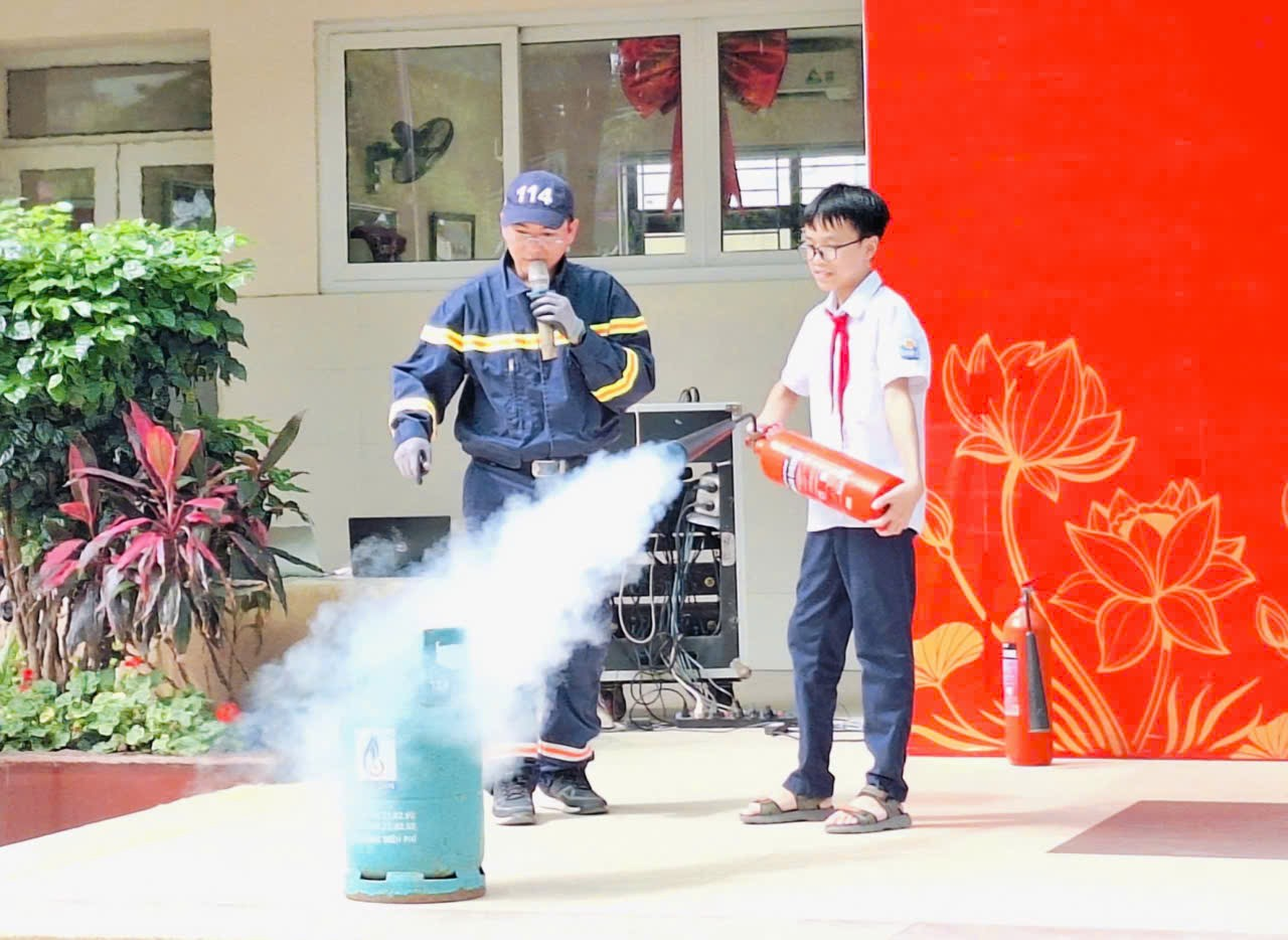 A person holding a fire extinguisher and a child standing next to a red wallDescription automatically generated