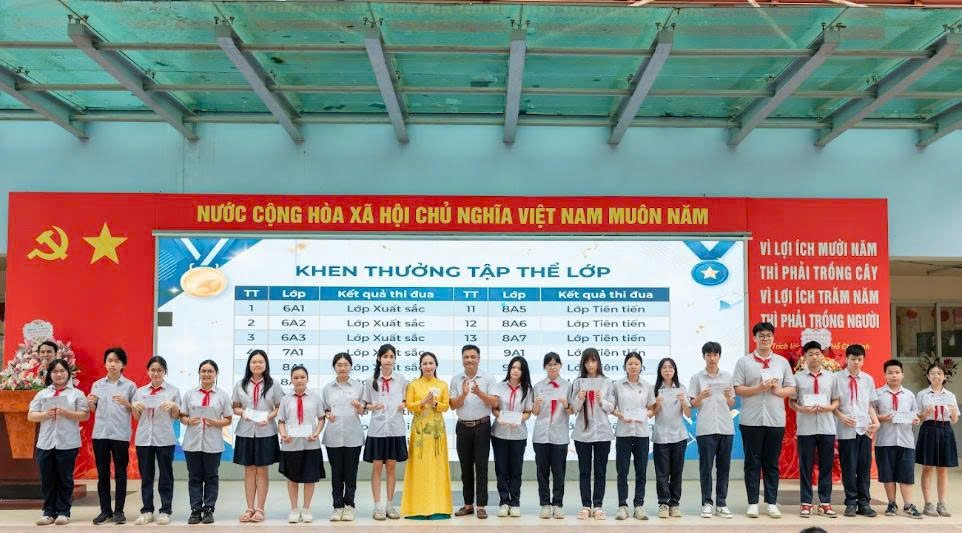 A group of people standing in front of a large screenDescription automatically generated