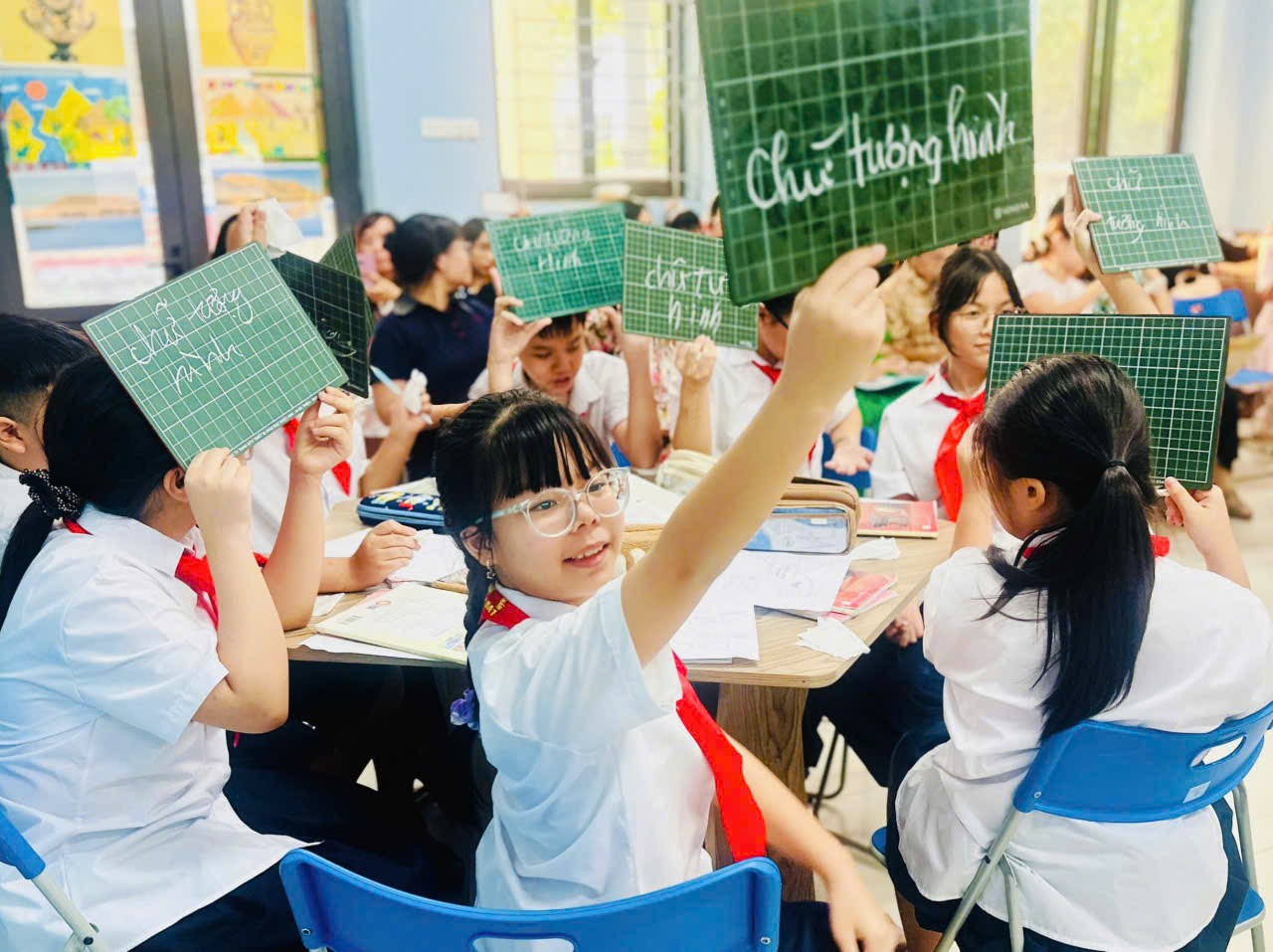 A group of children in a classroom holding up signsDescription automatically generated