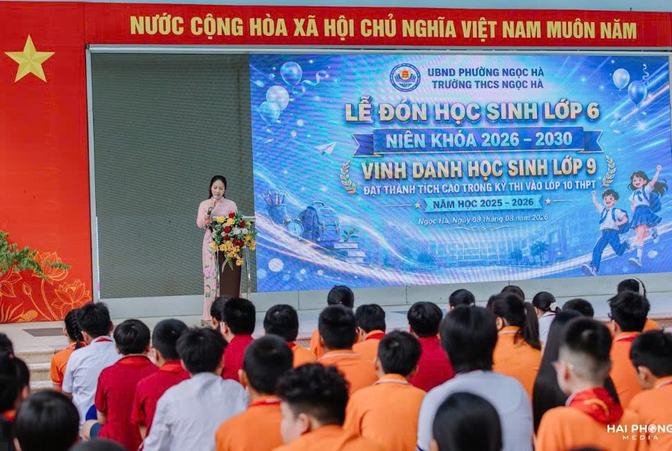 A person standing on a stage with a group of people in the background

Description automatically generated
