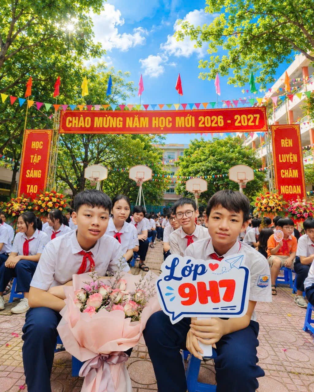 A group of boys in uniform sitting on chairs with flowers and a sign
Description automatically generated